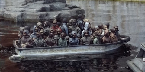 un bateau en métal gris vieilli rempli de nombreuses petites figurines détaillées de personnes exposé dans banksy dismaland