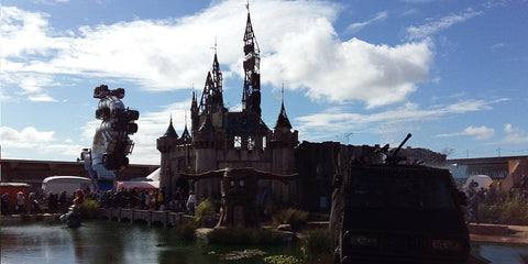 château de style gothique avec tours et flèches en pierre sombre sous un ciel partiellement nuageux dans larticle intitulé banksy dismaland.