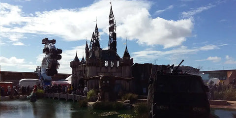 château de style gothique avec tours et flèches en pierre sombre sous un ciel partiellement nuageux dans larticle intitulé banksy dismaland.