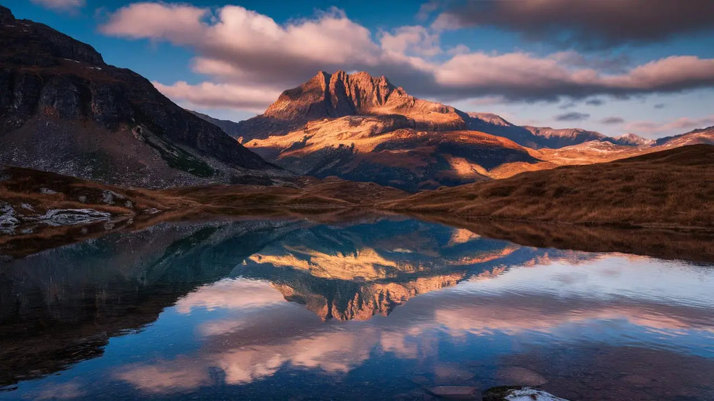 une toile personnalisée représentant un sommet de montagne majestueux et accidenté baigné de lumière dorée avec son reflet parfait dans un lac calme conçue à partir de vos photos préférées
